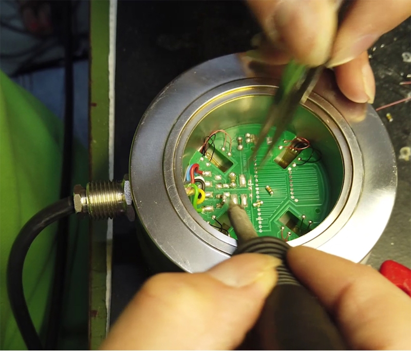 Cablagem de uma célula de carga: um operador fornece pontos de estanho nas almofadas dos extensômetros para conectar os fios elétricos.