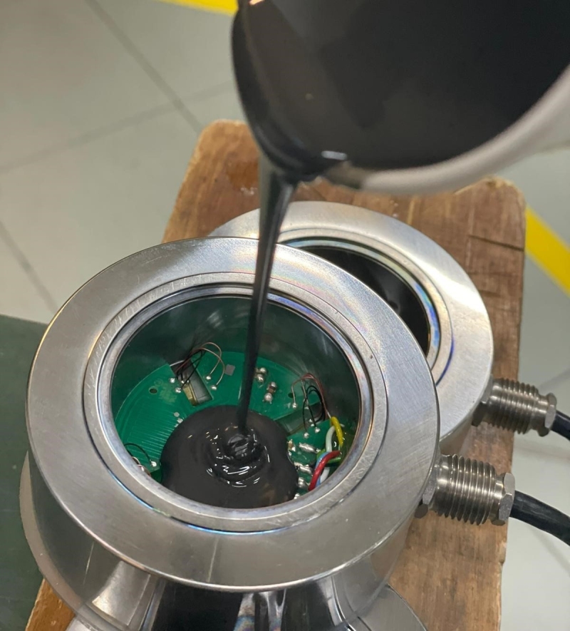 Resinagem da cavidade de uma célula de carga: a resina é despejada na cavidade até mergulhar completamente os extensômetros, os fios e a placa do PCB.